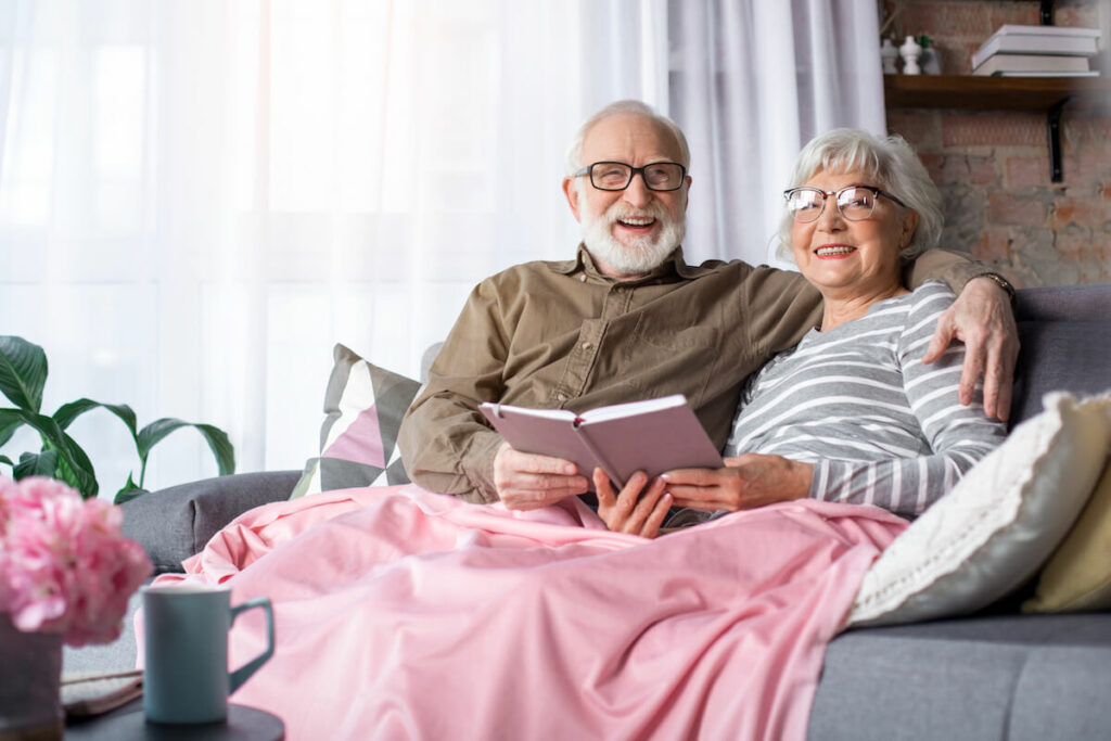 Avail Senior Living | Seniors reading on a couch with a pink blanket
