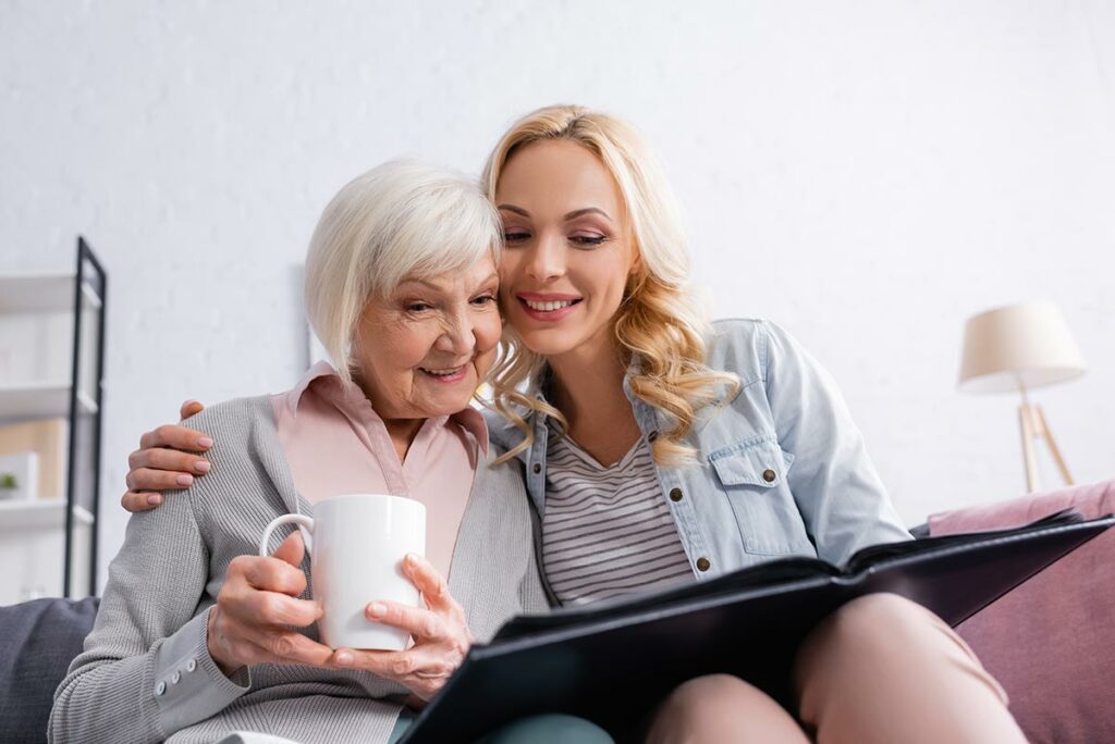 Avail Senior Living | Happy senior woman with caregiver looking at a photo album and drinking tea