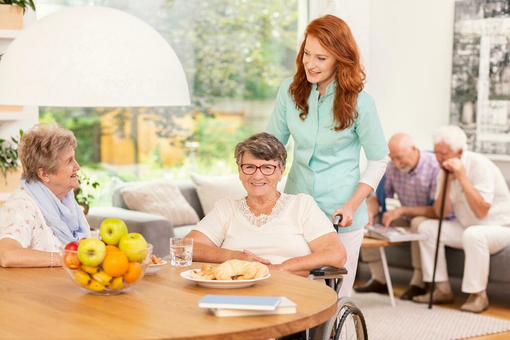 Avail Senior Living | Happy senior woman in wheelchair with caregiver eating breakfast with friends
